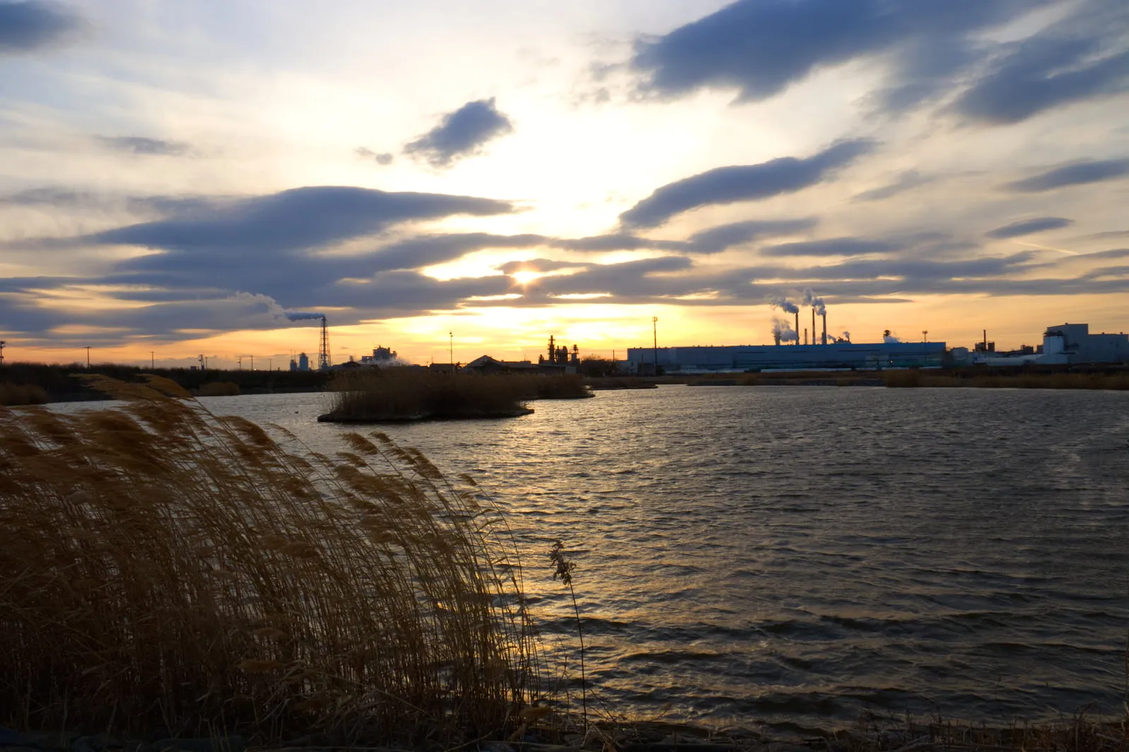 善海田池から見る夕陽と、工場の煙突からのぼる煙の写真