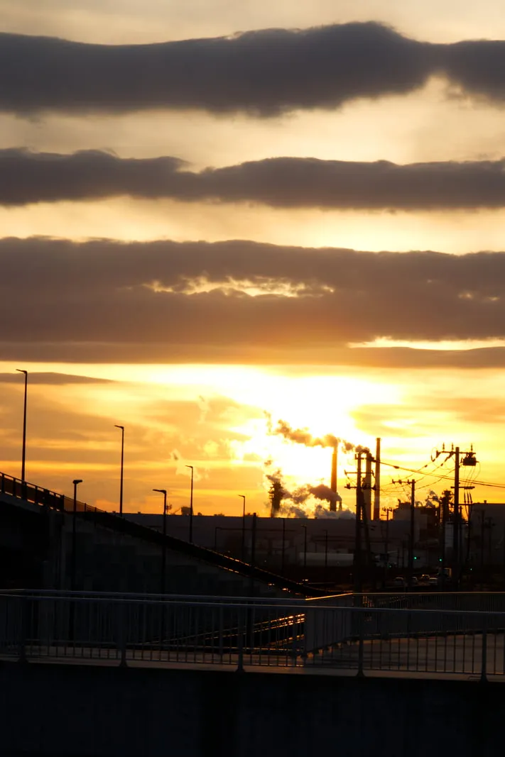 工場の煙突からのぼる煙と夕陽の写真